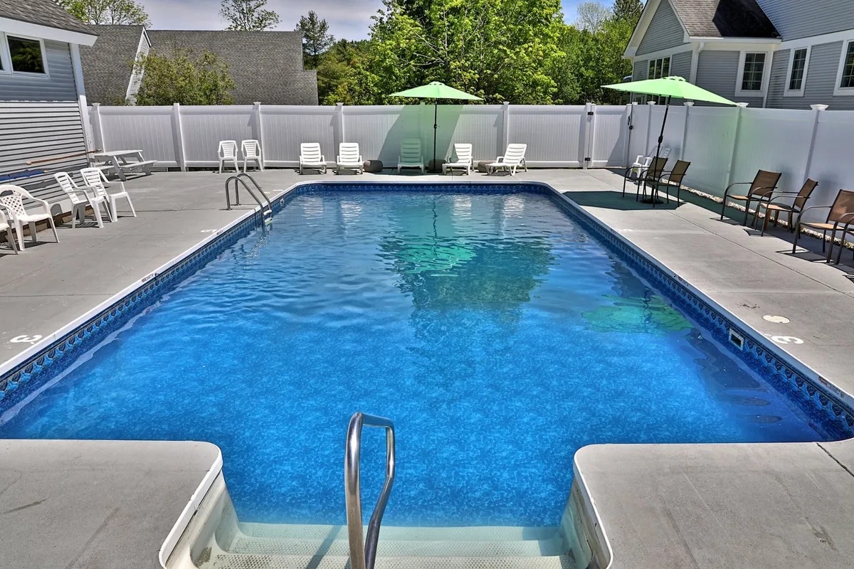 An inviting exterior shot of the property’s fenced outdoor swimming pool, surrounded by lounge chairs and green umbrellas. The poolside setting is ideal for relaxing, sunbathing, and socializing during warm summer days.