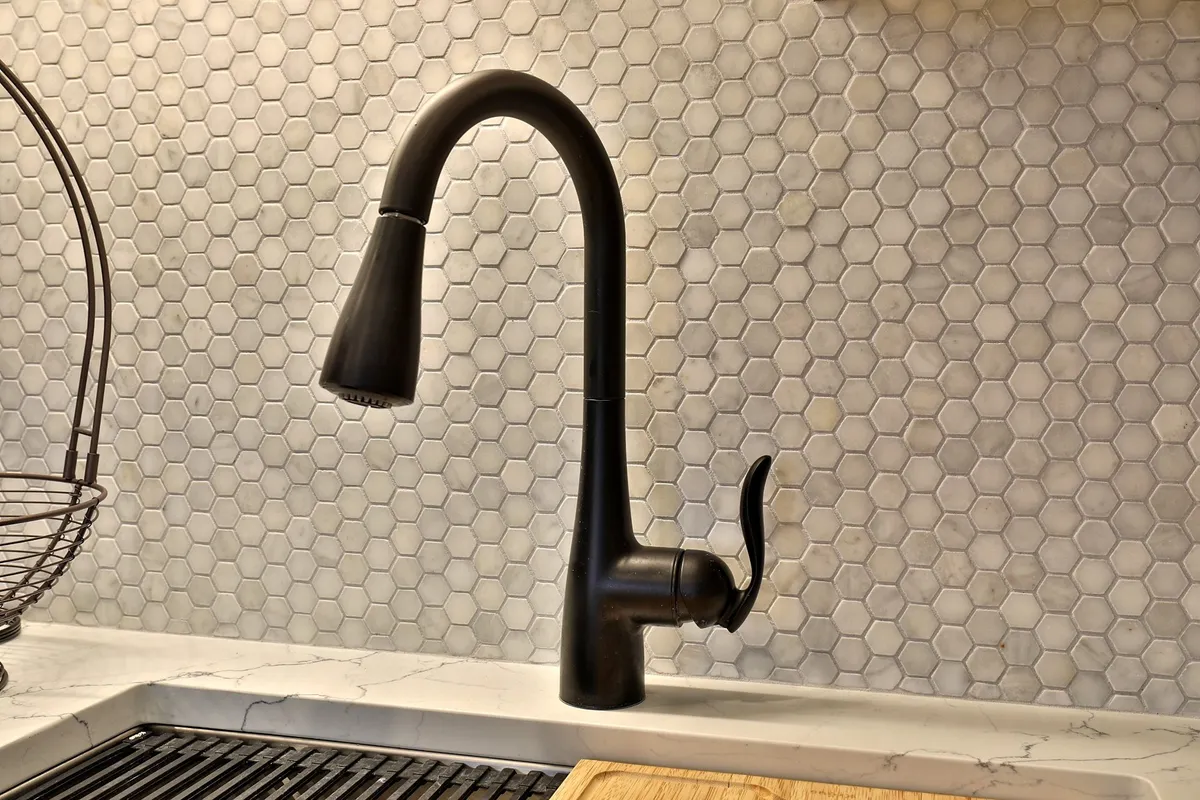 A sleek kitchen space featuring a black faucet, hexagonal backsplash, marble countertop, and wooden cutting board. The ambiance is contemporary and inviting, hinting at both productivity (preparing meals during work breaks) and moments of relaxation or socializing after work hours.