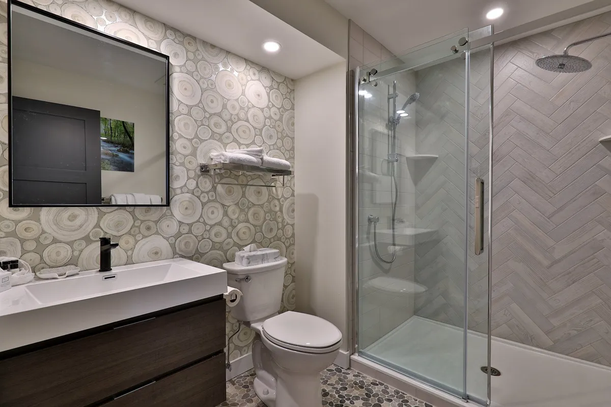 A bright bathroom with a large mirror, modern stylish sink, and a glimpse of the shower area. Decorative touches on the wall and smart lighting create a fresh, inviting atmosphere ideal for personal grooming and relaxation.