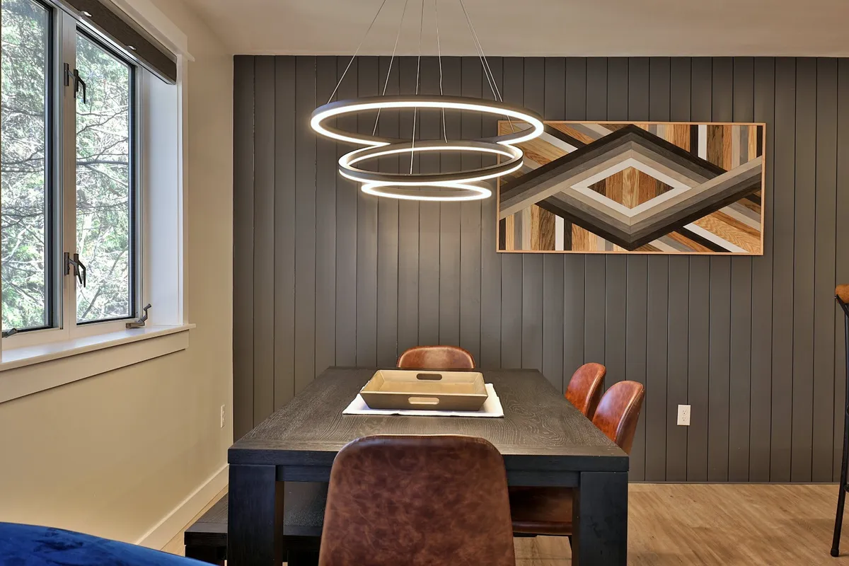 A stylish dining area with a modern pendant light, elegant dining table, comfortable leather chairs, and vibrant wall art. The setting is perfect for family dinners, casual meals, or artistic conversations, radiating a contemporary and cozy ambiance.