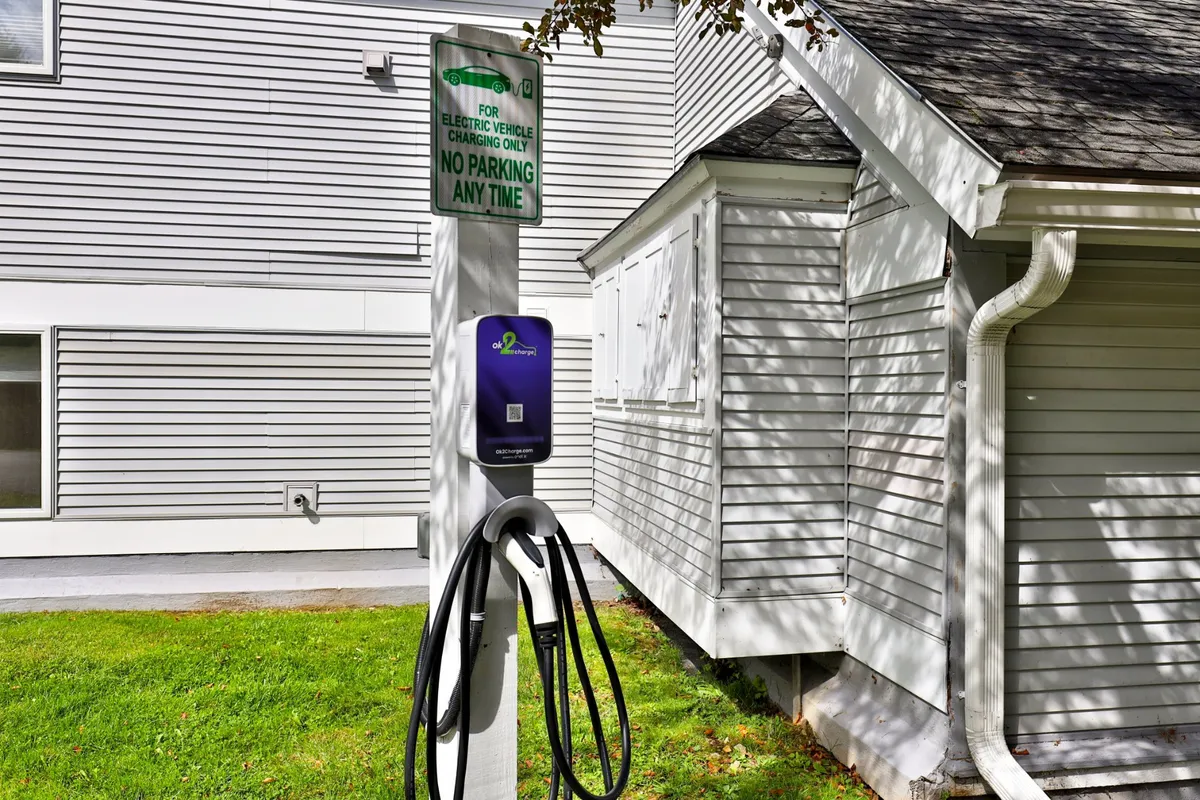 This exterior shot displays an electric vehicle charging station with clear signage, set against the backdrop of the community. The scene communicates a blend of modern amenities and eco-friendly values.